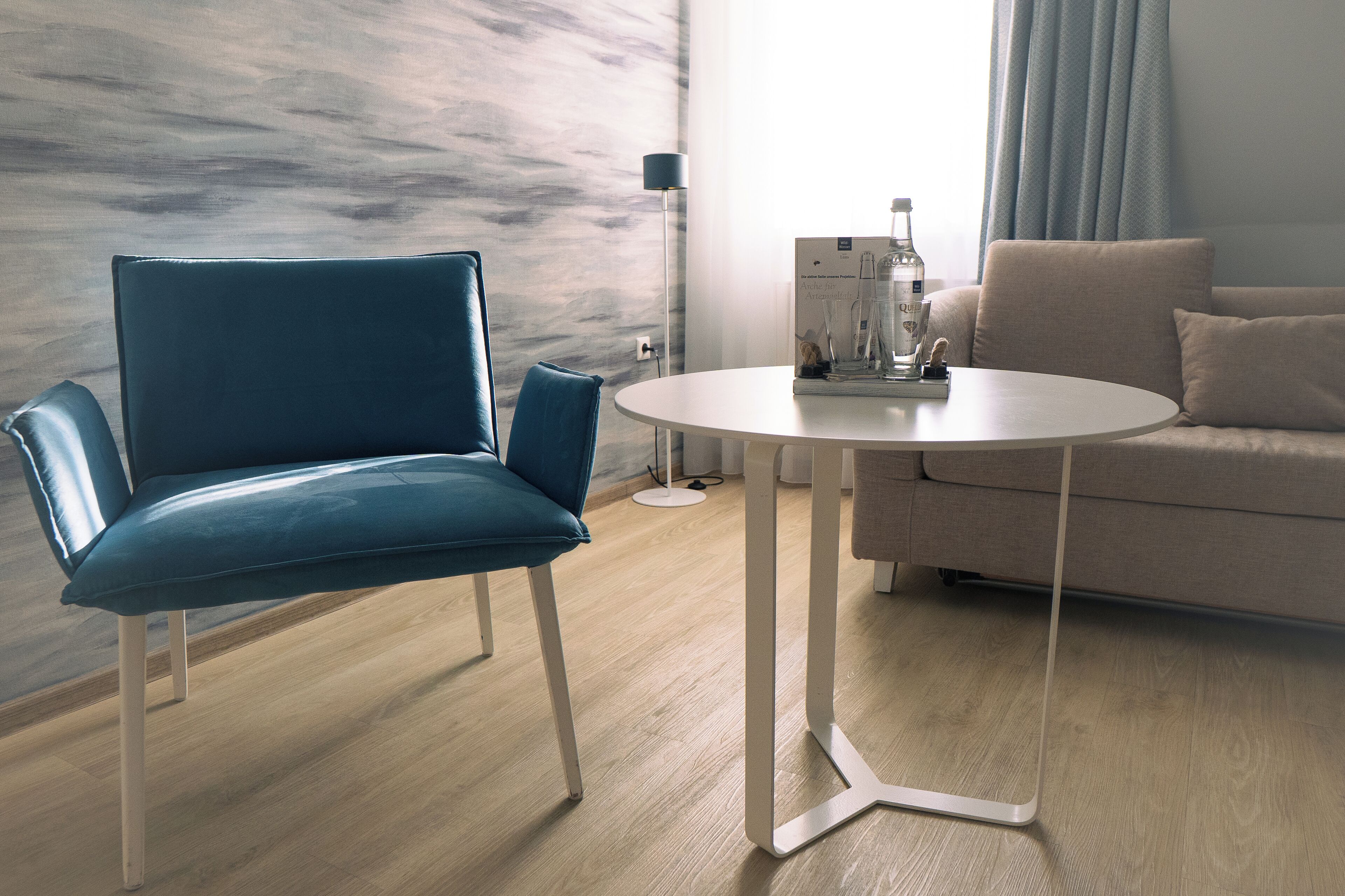 Ein modernes Zimmer mit blauem Sessel, rundem Tisch und einer Couch.