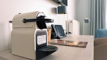 Een Nespresso koffiemachine op een houten tafel, met een tijdschrift en een lamp op de achtergrond.
