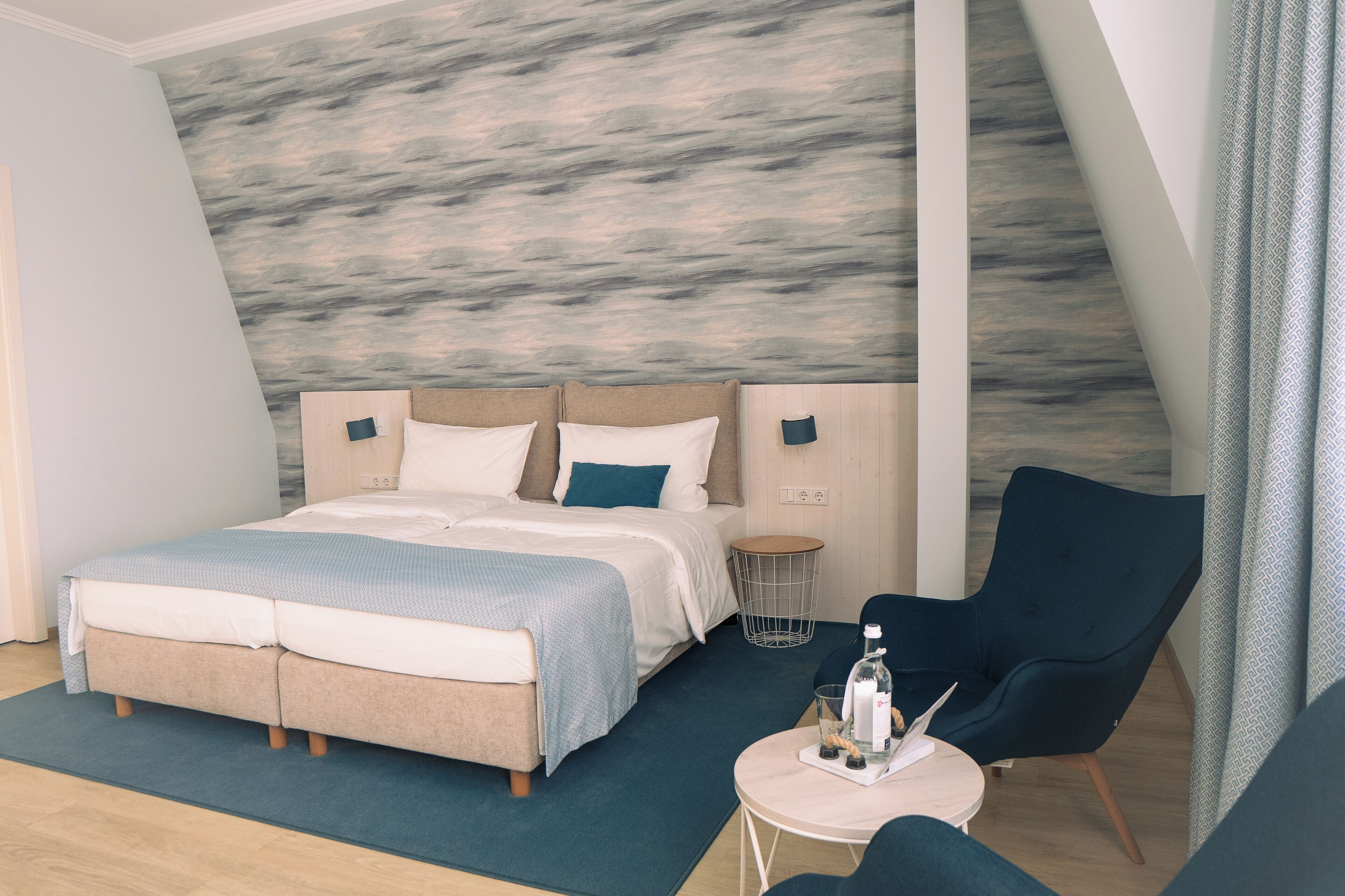 Un dormitorio moderno con una cama grande, una mesita redonda y un sillón oscuro.