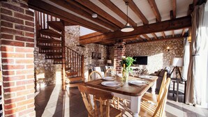 A dining area with a wooden table set for four, surrounded by wooden chairs, in a rustic stone-walled room with exposed wooden beams.