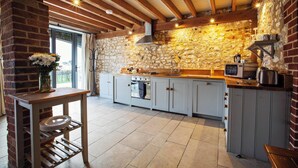 A rustic kitchen with exposed wooden beams, a stone wall, and a built-in oven.