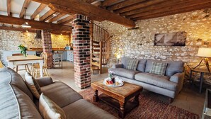 A cozy living room with a stone wall, a fireplace, and a staircase leading to a kitchen.
