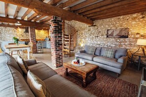 Ein gemütliches Wohnzimmer mit Steinwand, Kamin und Treppe, die zur Küche führt.
