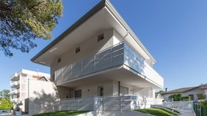 A modern two-story residential building with a flat roof, large windows, and a balcony. - Modern Apartment With Shared Pool (San Michele al Tagliamento)
