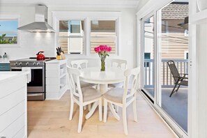 A modern kitchen with white cabinetry, a gas stove, and a dining area with white chairs and a vase of flowers. - Stylish 3BR Beach Condo w/ Vaulted Ceilings – One Block to Ocean (Ocean City)