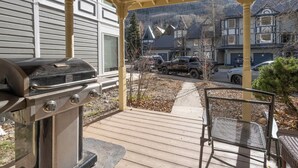 Ein überdachter Außenbereich mit Grill, einer Holzterrasse und Blick auf eine Wohngegend.