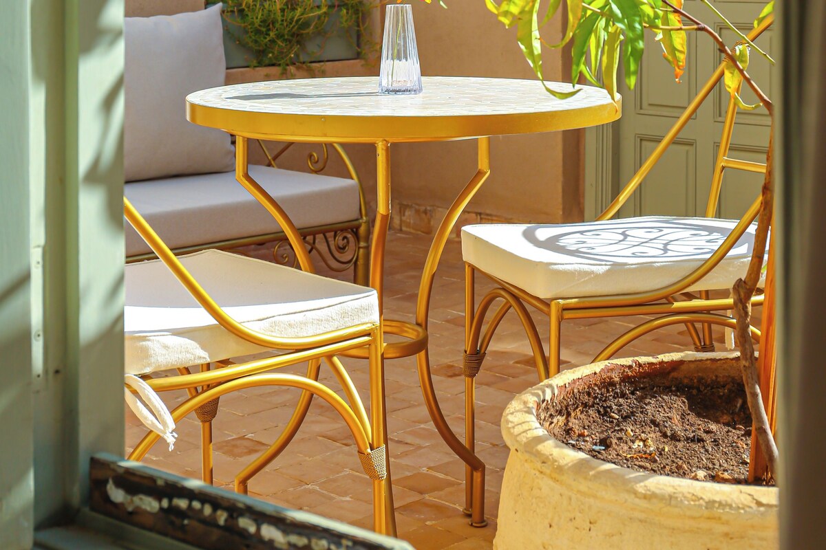A patio with a round table, two chairs, a potted plant, and a door.