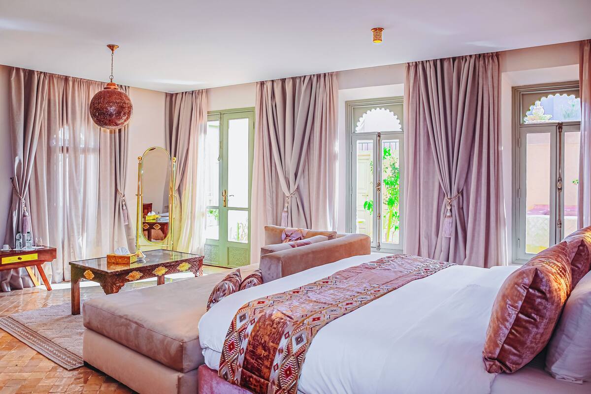 Een slaapkamer met een groot bed, een zithoek, een kaptafel met spiegel en uitzicht op groen.