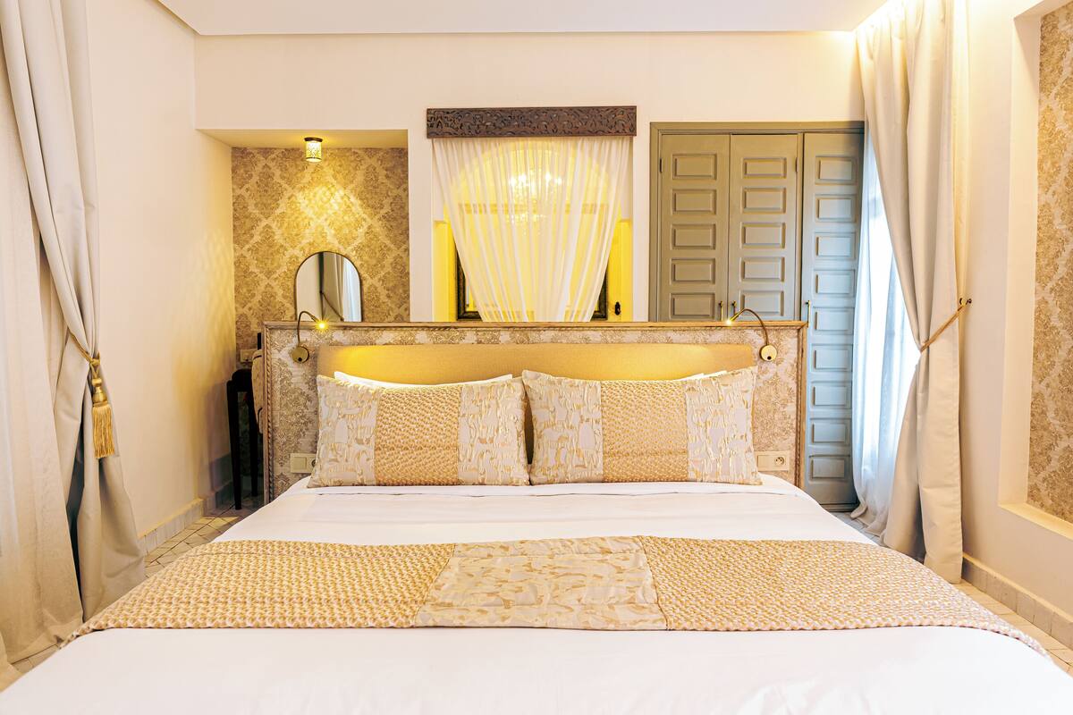 Een hotelkamer met een bed, een spiegel, een deur en een raam met gordijnen.