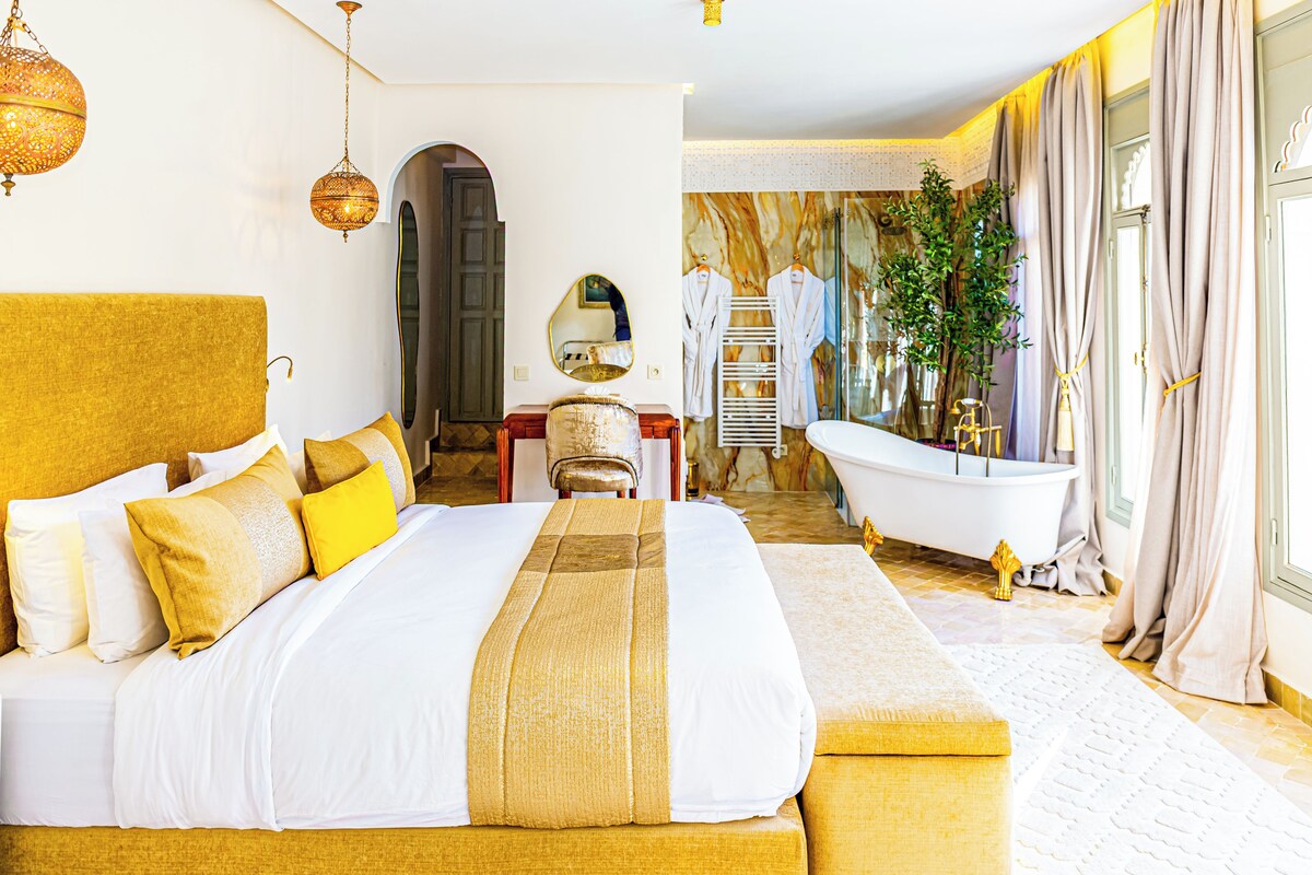 A large bed with a headboard, a sitting area, a bathtub, and a mirror.