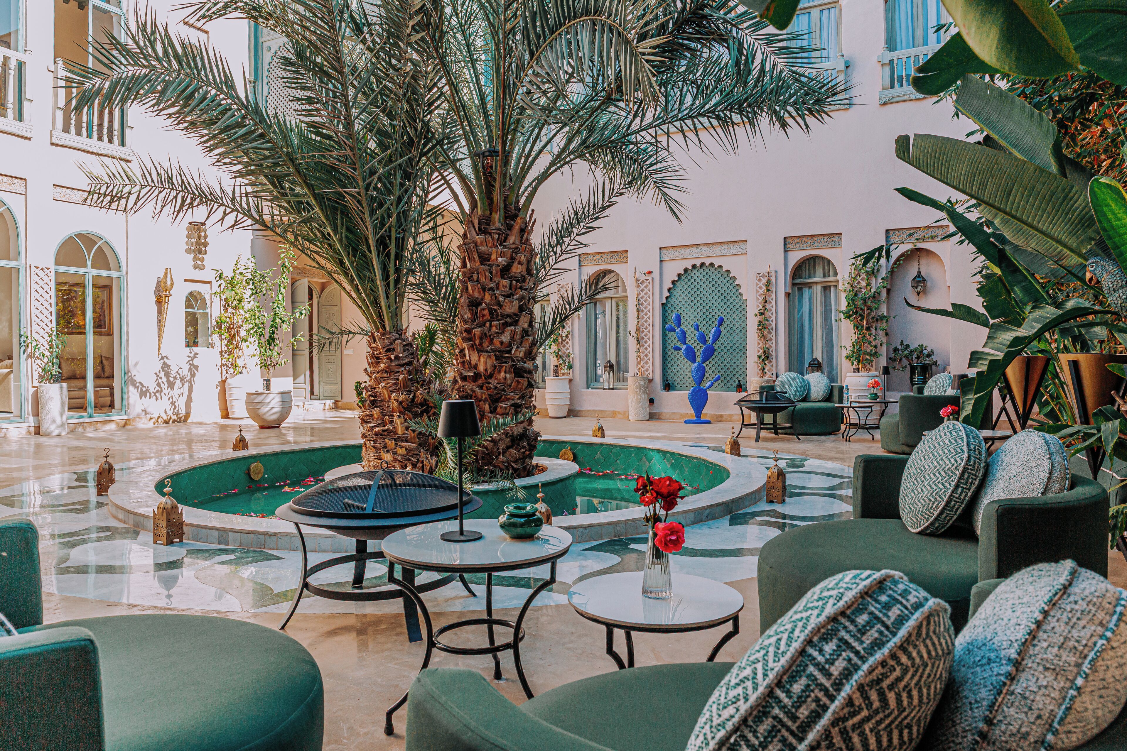Un espacio interior amplio con una palmera central, varios conjuntos de asientos y una piscina decorativa.