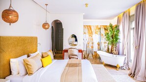 A spacious bedroom with a large bed, a sitting area, a bathtub, and a view of a cityscape. - Kasbah La Moun The Art of Hospitality (Marrakech)