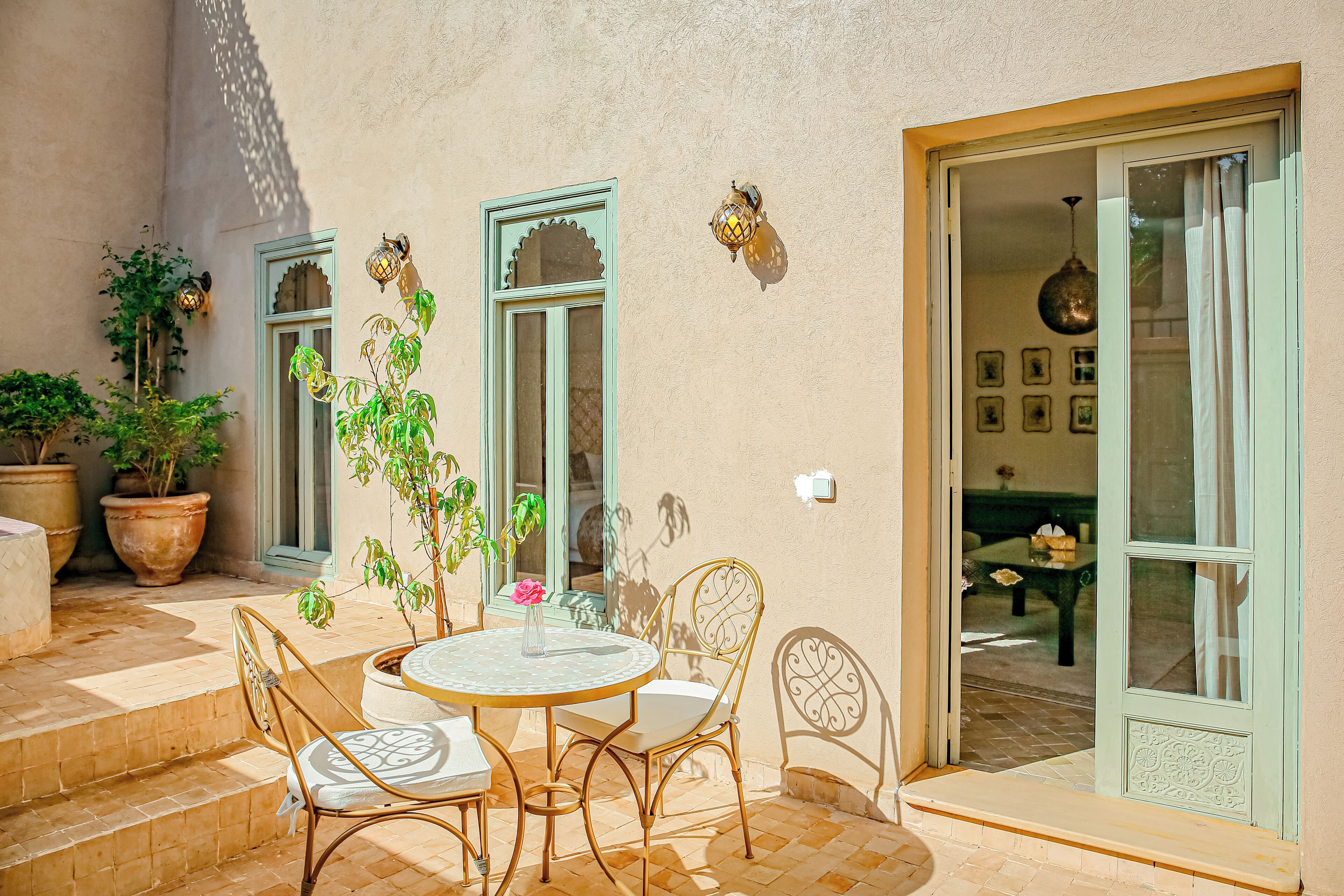 Une terrasse extérieure avec une table ronde et des chaises, des plantes en pot et une porte-fenêtre coulissante donnant sur un espace intérieur.