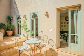 An outdoor patio with a round table and chairs, potted plants, and a sliding glass door leading to an interior space. - Kasbah La Moun The Art of Hospitality (Marrakech)