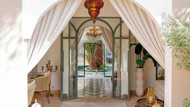 An arched doorway with a chandelier, a palm tree, and a dining area with a table and chairs. - Kasbah La Moun The Art of Hospitality (Marrakech)