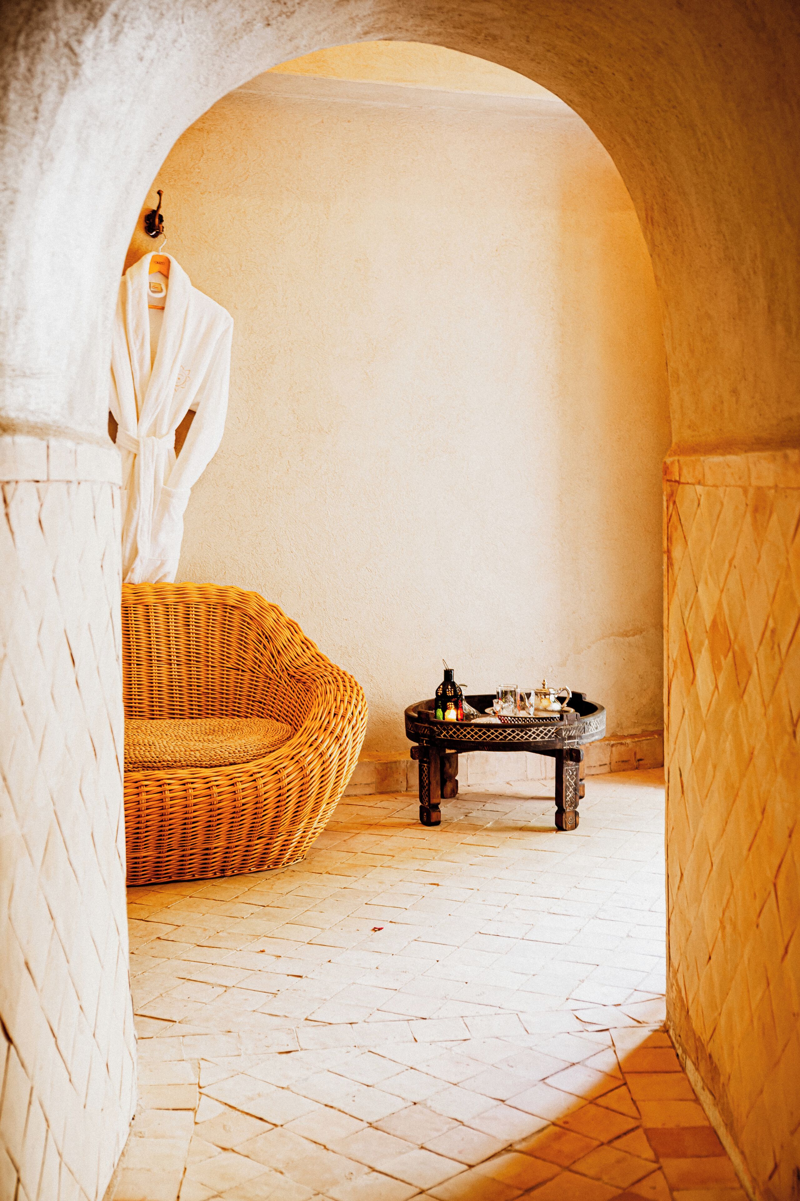 A spa area with a wicker chair, a small table with a bottle and glass, and a robe hanging on a hook.