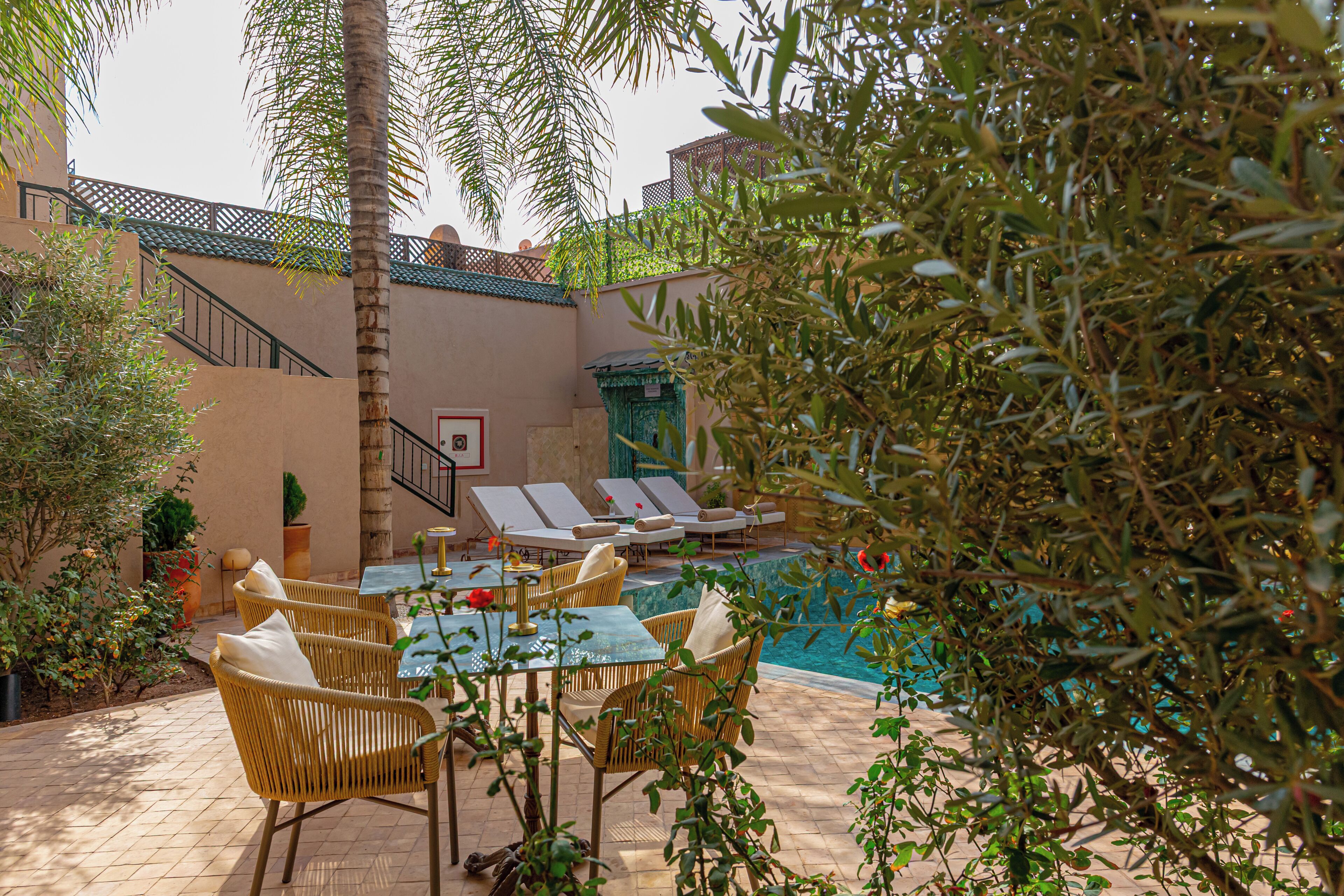 Un espace aménagé au bord de la piscine, avec des chaises longues, une table et un escalier menant à un niveau supérieur.