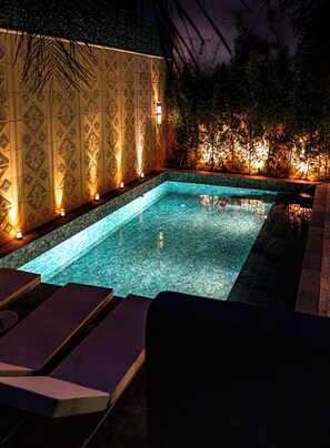 A rectangular swimming pool with a tiled edge, surrounded by lounge chairs and wall-mounted lights. - Kasbah La Moun The Art of Hospitality (Marrakech)