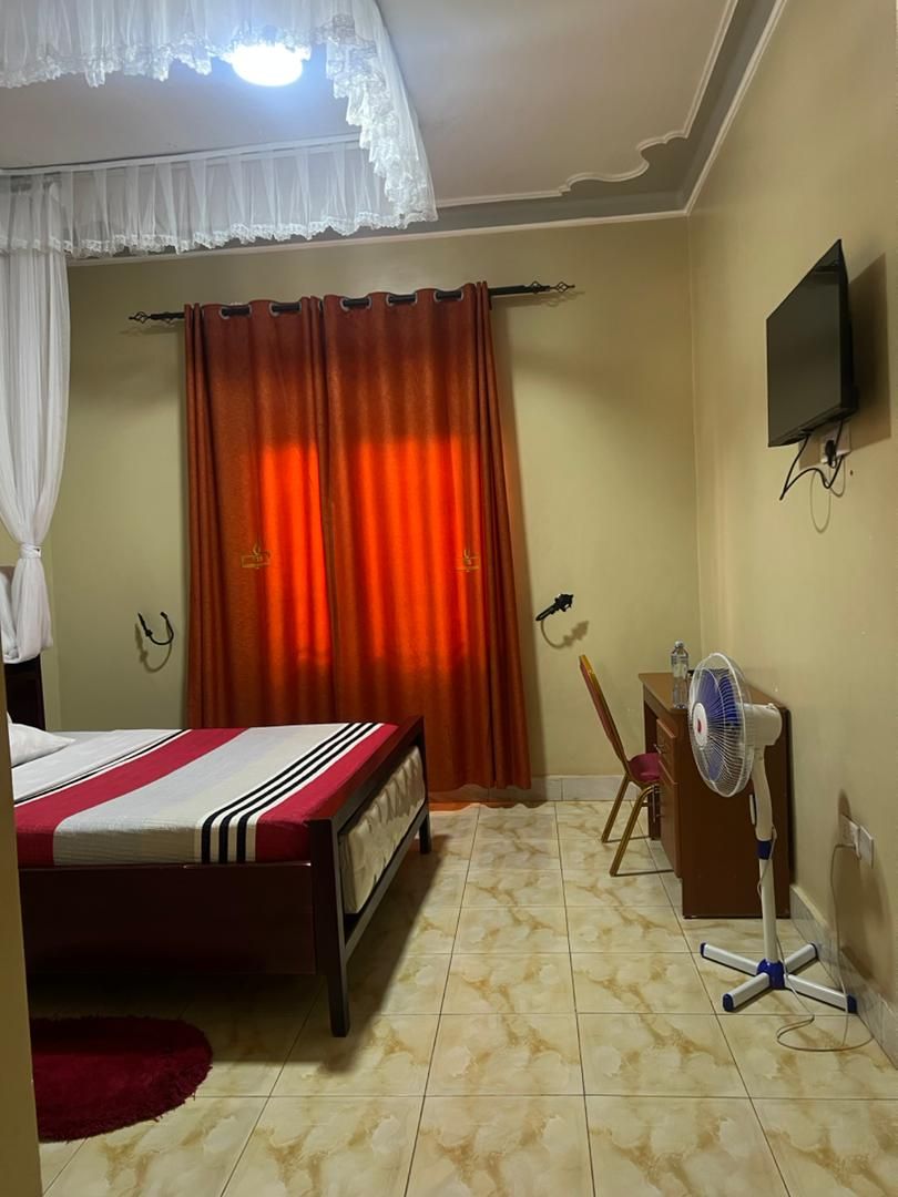 A bedroom with a bed, curtains, a TV, a fan, and a desk.