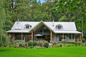 A modern house with a large front porch, a covered outdoor area, and a well-maintained garden. - Waldenbrook - Luxury in the woods (Bundewallah)