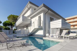 Ein modernes, zweistöckiges Gebäude mit Schwimmbad, Außenbereich und weißem Zaun.