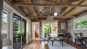 Una habitación amplia con suelo de madera, un ventanal grande y un techo con vigas a la vista.