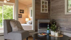 Una habitación acogedora con una cama, un sillón gris, una mesa redonda con un plato de comida y una botella de agua.