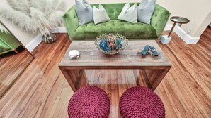 A green sofa with grey cushions, a wooden coffee table with a decorative bowl and remotes, and two red poufs on a wooden floor. - Comfort Meets Convenience – 3BR + Free Parking (Boston)