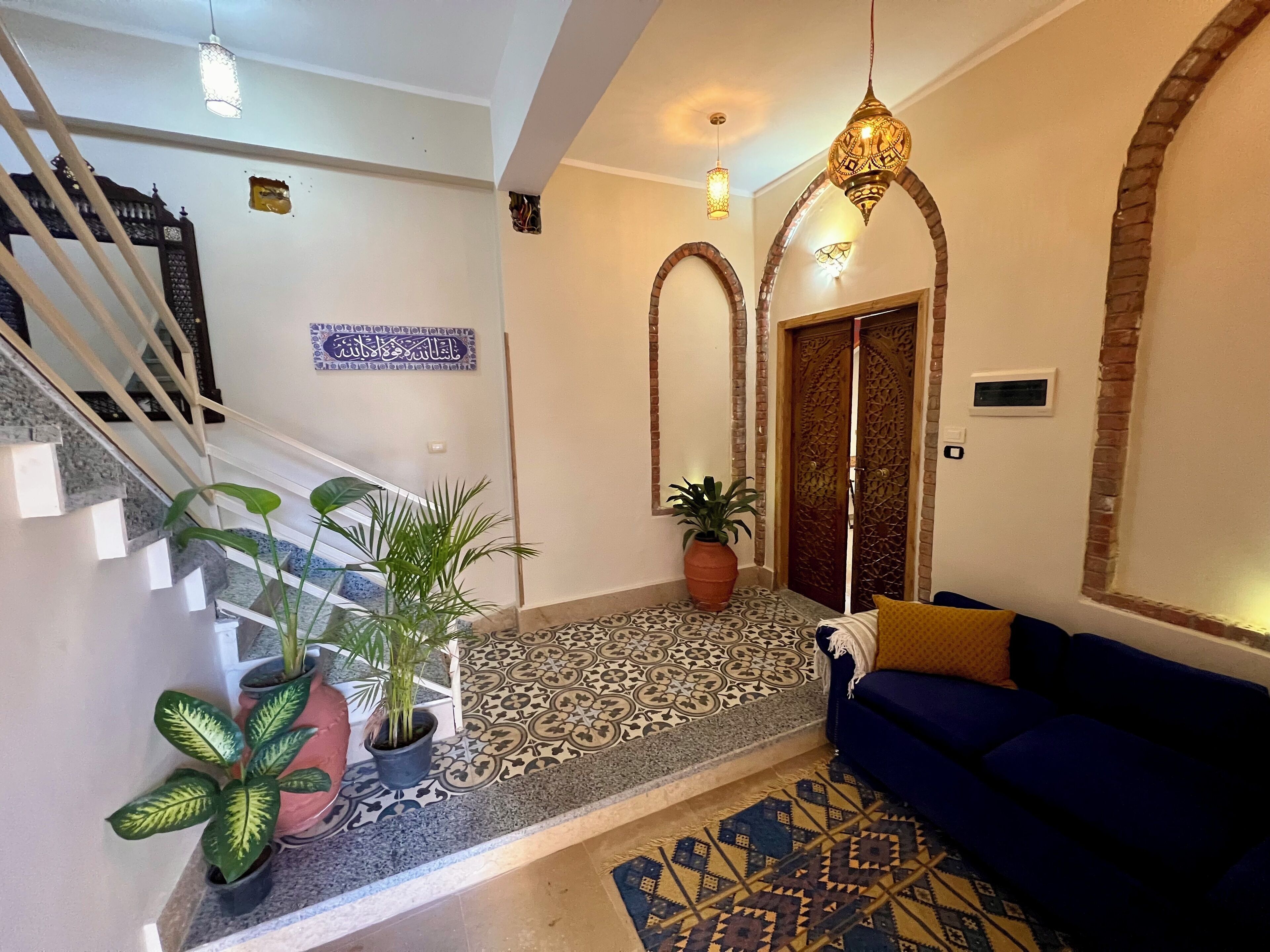 A modern interior with a staircase, a blue sofa, patterned flooring, and decorative lighting.