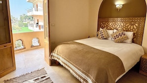 A bedroom with a large bed, a view through an open door to an outdoor balcony, and a decorative ceiling light. - Charming deluxe villa, family atmosphere in the authentic West Bank of Luxor (Luxor Governorate)