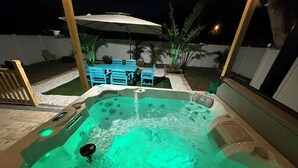 Ein Whirlpool mit grünem Licht, umgeben von Gartenmöbeln und Pflanzen.