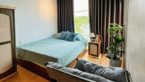 A bedroom with a bed, a small table, a plant, and a window with curtains. - RUBY HOTEL FRONT OF BEACH 2 (Tien Thanh)