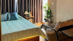A bedroom with a bed, a chair, a nightstand, and a window with curtains. - RUBY HOTEL FRONT OF BEACH 2 (Tien Thanh)