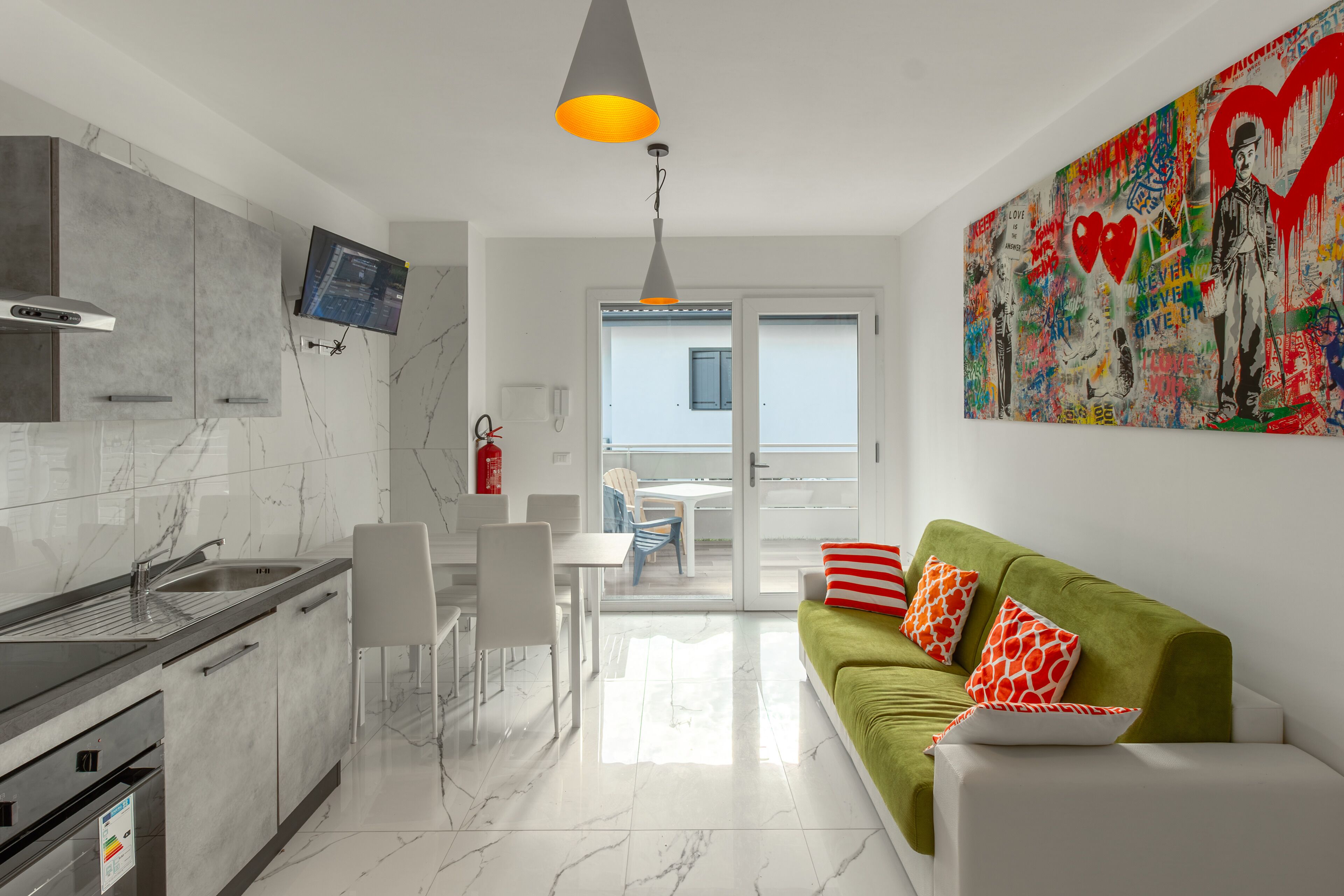 Una cocina moderna con estufa integrada, un comedor con mesa y sillas, y un sofá verde con almohadas rojas y blancas.