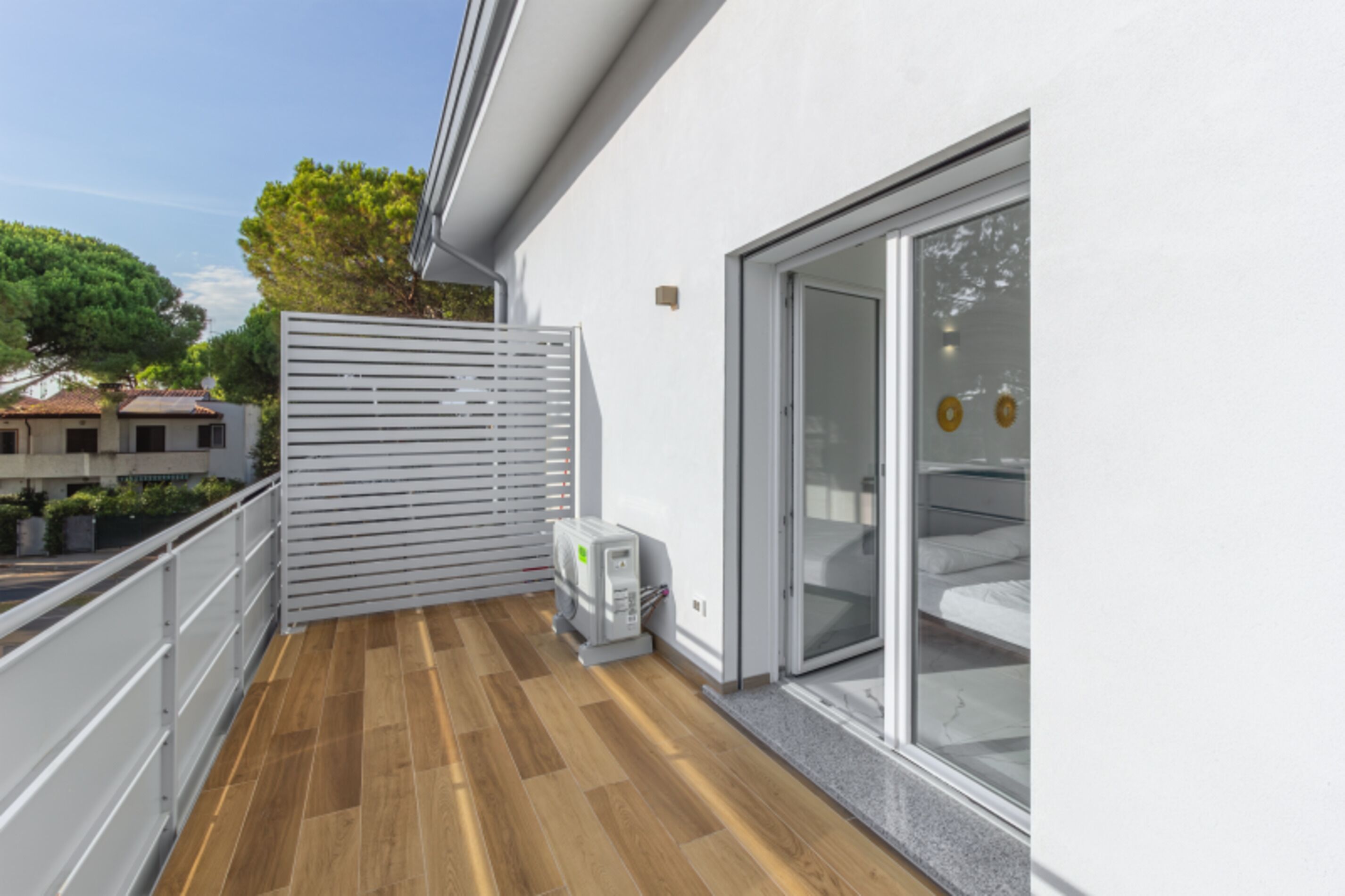 Un balcon doté d’un plancher en bois, d’une balustrade blanche et d’une porte vitrée donnant sur une pièce où se trouve un lit.