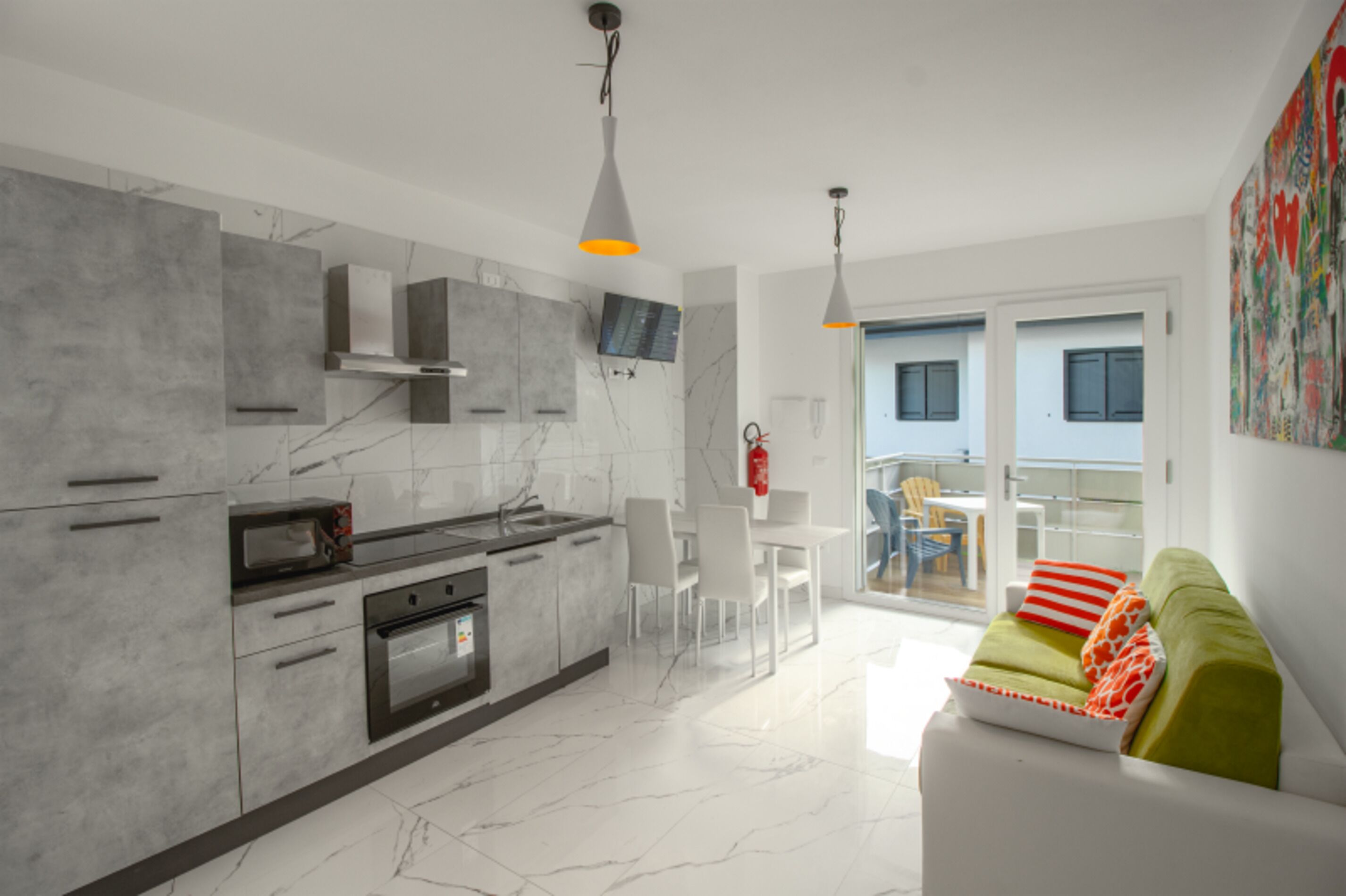 A modern kitchen with marble countertops, a built-in oven, and a dining area with a white table and chairs.