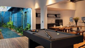 Una mesa de billar con taco y bolas, una terraza de madera y una zona de cocina con fregadero y encimera.