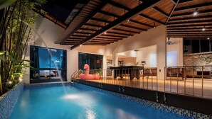Una piscina con borde de azulejos, una terraza de madera y un muro de piedra.