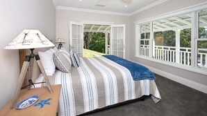 Une chambre à coucher comprenant un lit, un ventilateur de plafond, une table de chevet avec une lampe, et une vue sur l’extérieur grâce à de grandes fenêtres.