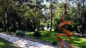 Une sculpture métallique dans un jardin, avec un chemin de pierre et des arbres.