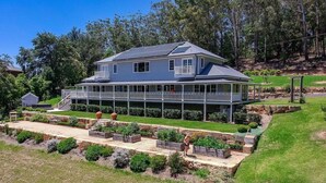 Une maison à deux étages dotée d’un balcon, entourée d’un jardin bien entretenu et d’arbres.