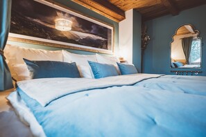Une chambre à coucher avec un grand lit, un tableau représentant un paysage de montagne, un miroir et un plafond en bois.