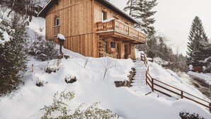 Uma cabana de madeira com varanda, rodeada por árvores cobertas de neve e um cercado de madeira.