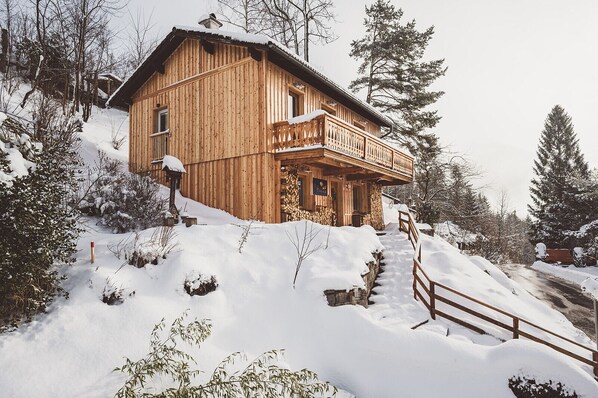 Une cabane en bois dotée d’un balcon, entourée d’arbres couverts de neige et d’une clôture en bois.