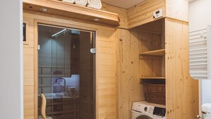 Uma sala de sauna com paredes de madeira, porta de vidro, máquina de lavar e pia.