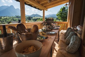 Une terrasse en bois avec une table dressée pour le repas, offrant une vue sur un paysage montagneux.