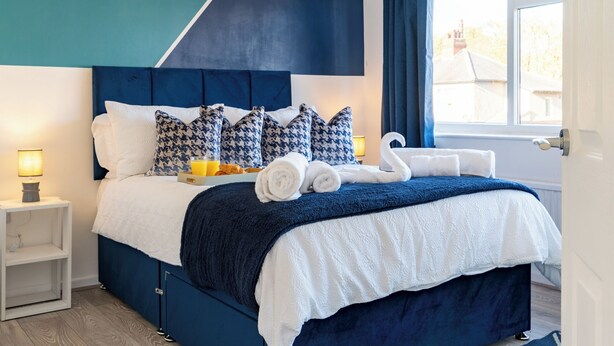 A neatly made bed with a blue headboard, white bedding, and decorative pillows. - Headingley Lodge - Modern Home Near City Centre (Leeds)