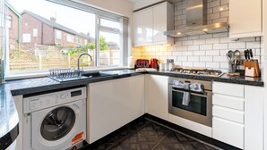 A compact kitchen with a washing machine, a stove, and a sink. - Headingley Lodge - Modern Home Near City Centre (Leeds)