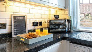 A breakfast setup with a tray of croissants and orange juice, a digital clock, and a menu board listing specials and extra items. - Headingley Lodge - Modern Home Near City Centre (Leeds)