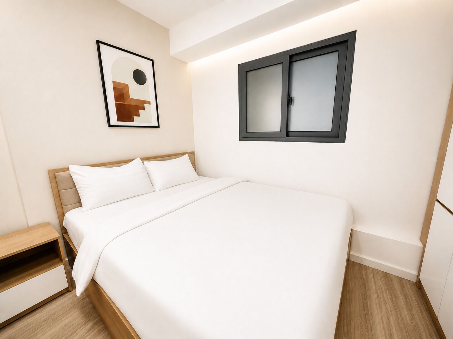 A neatly arranged bedroom with a bed, a bedside table, a framed picture on the wall, and a window with blinds.